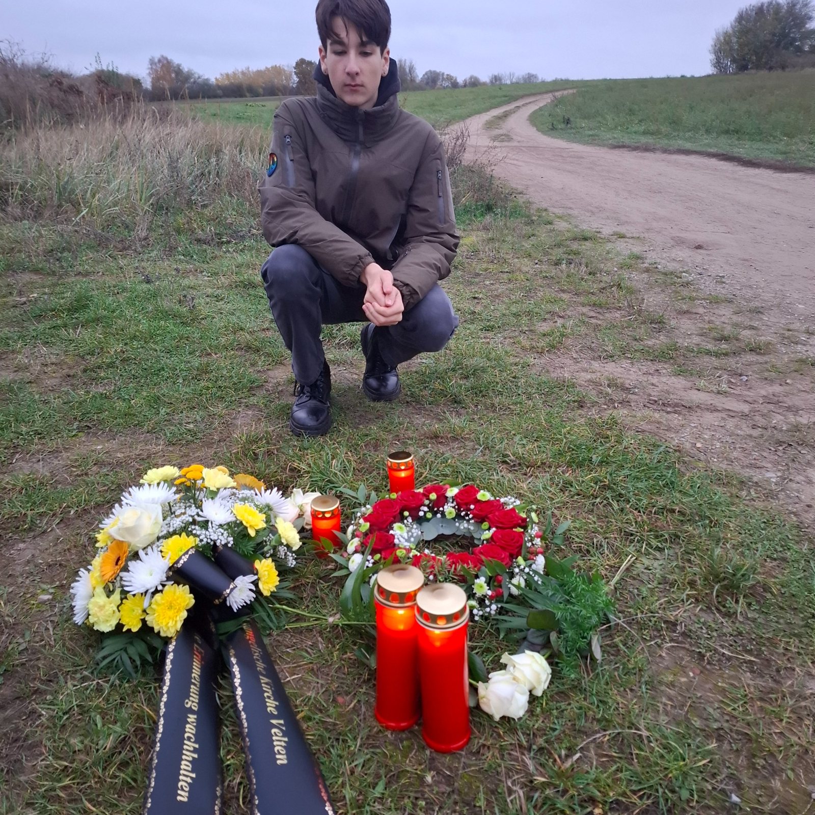 Kranz und Kerzen am Gedenkort in Velten, ein junger Mann kniet davor